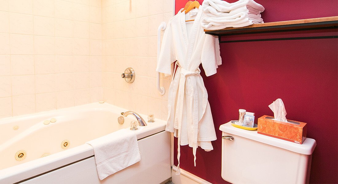 Bathroom decorated in rich red with white trim, white shower with tub basin. White robes hang on the wall.