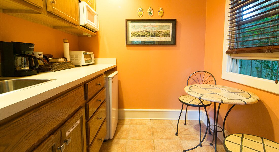 A warm yellow kitchen with appliances on counter across from table underneath window.
