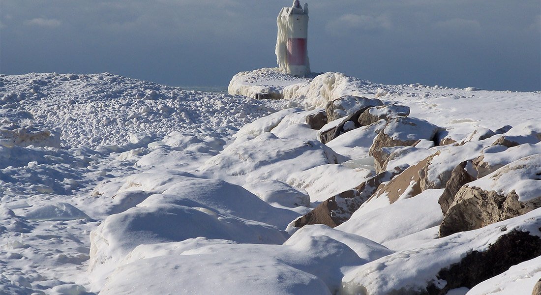 A snowcovered winterscape: Ice and snow over rocks landscape. Ice gives lighthouse a glazed appearance.