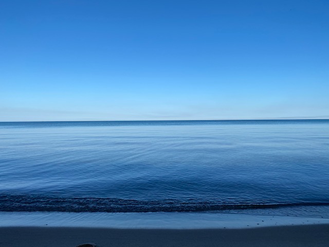 Ripples across the surface of the ocean underneath a crystal clear blue sky with the slightest fade of clouds upon the horizon. 