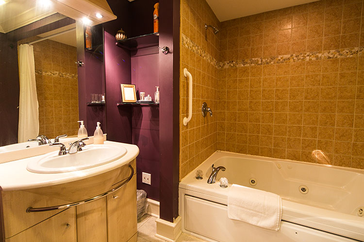 Jetted tub with grab bar and decorative tile backsplash and unique rounded vanity and lights.