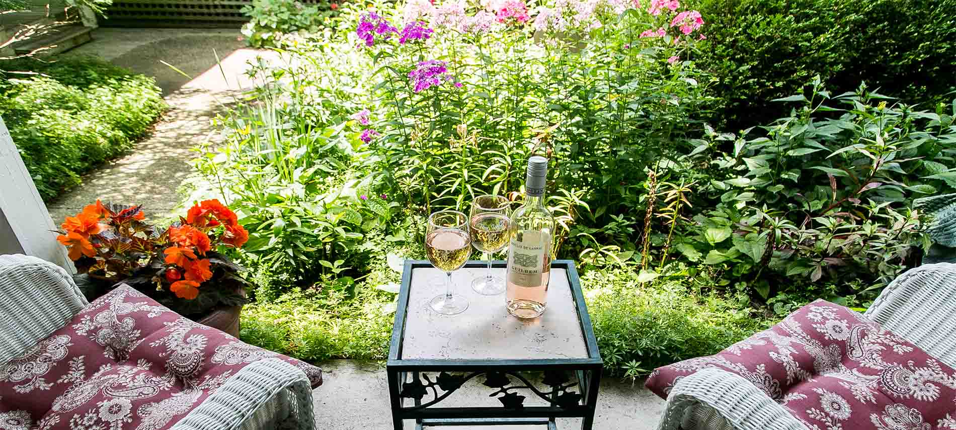 Table with two wine glasses and bottle of pink wine. Wicker chairs sitting next to it.
