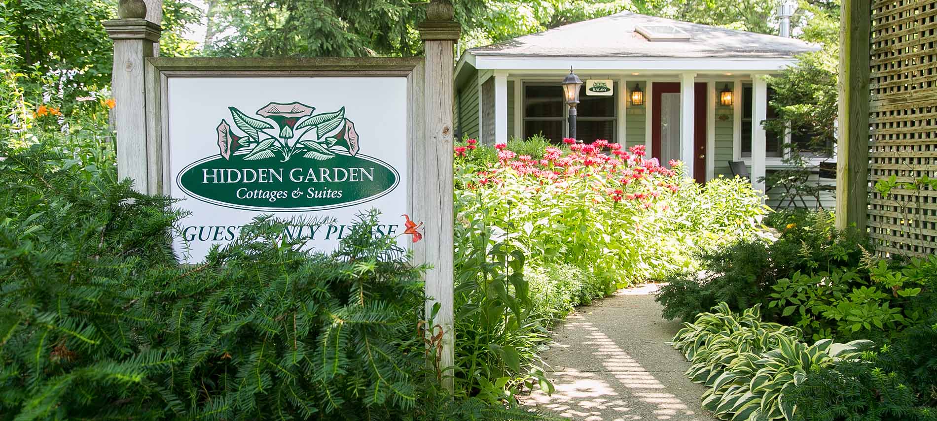 Cottage with Guest Only sign up front, lots of red flowers around the front door.