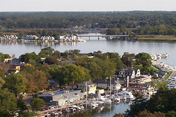 Riverfront view over pier with boats, across a river to more piers and rich wooded background. Link leads to Thing-to-Do