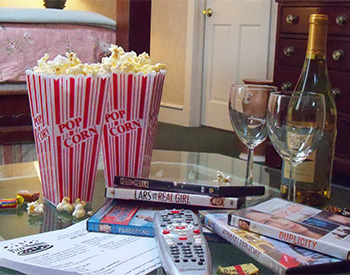 Popcorn, movies, remote, and wine sitting on a glass table in front of bed.