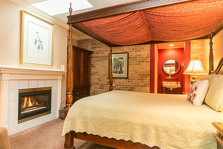 Oak four poster bed with canopy and fireplace. Bed has cream duvet and red canopy.