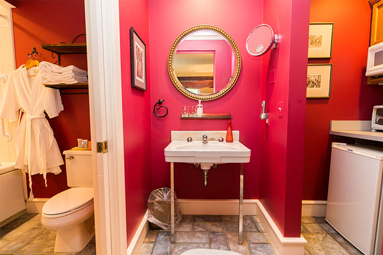 Bathroom with red walls sinkm toilet, robes, towels, mini-fridge, and microwave.