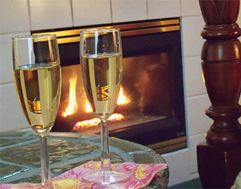 Full champange glasses in front of roaring fireplace on glass table.