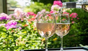 Wine being poured into two wine glasses with a backdrop of flowers.