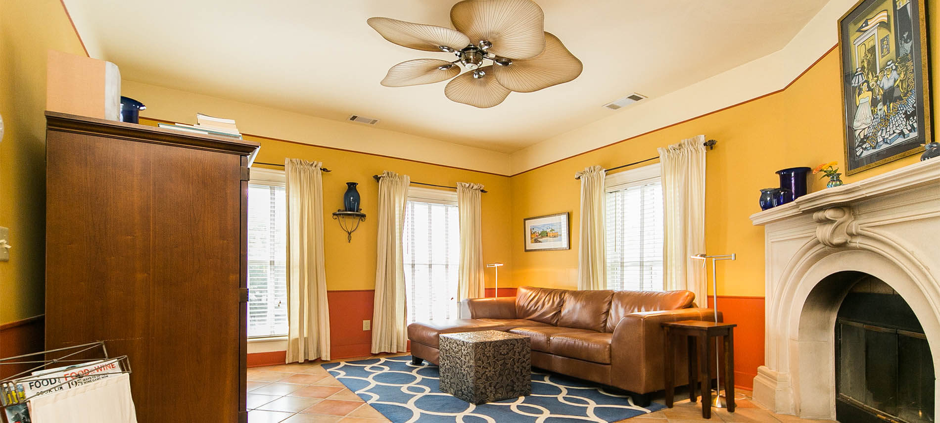 Brown leather couch with blue run that had round rings in it and a white stone fireplace and unique fan.