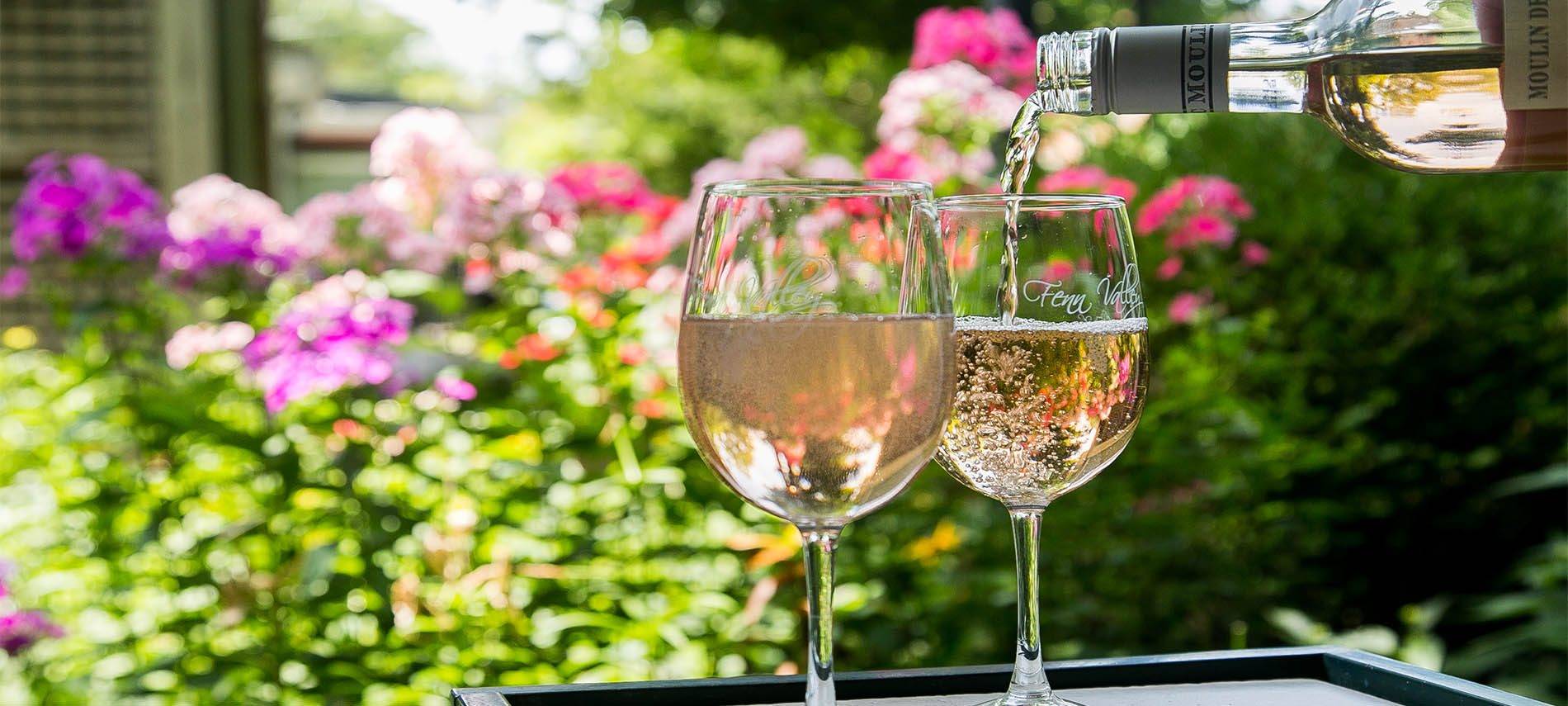 Wine being poured into two wine glasses with a backdrop of flowers.