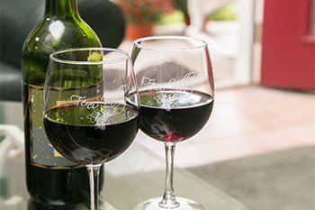 Wine bottle and two glasses of wine on a counter top in front an open red door leading outside.