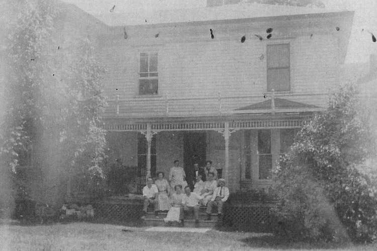 Old photo of family and friends sitting on front porch with arms around each other.