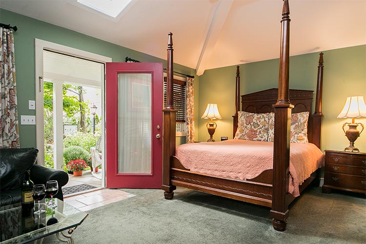 Four poster bed with peach comforter and flowered bed pillows. Leather couch in the corner.